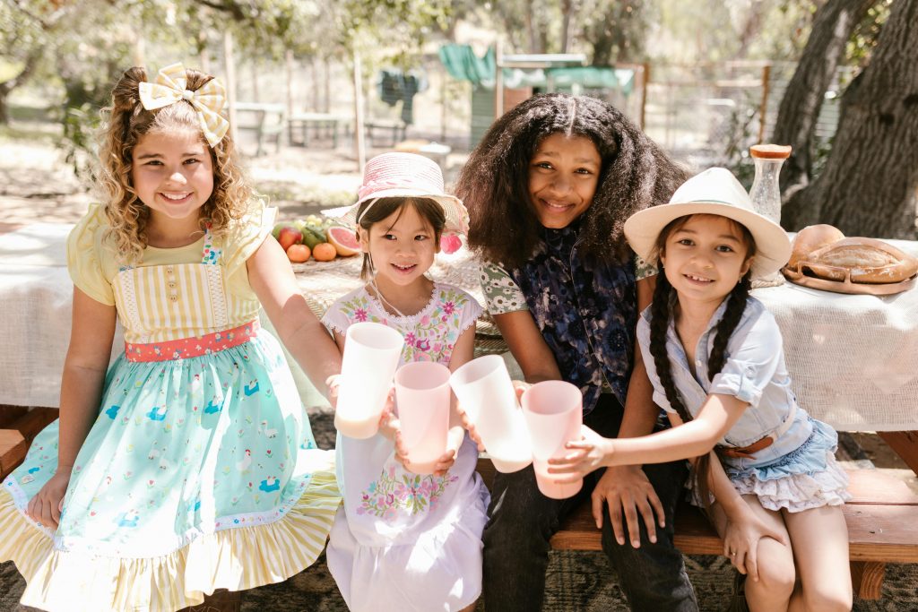 Four children smiling and holding cups at an outdoor picnic table.